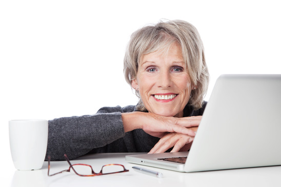Smiling old woman resting on the table with laptop and cup of coffee