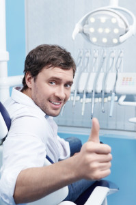 A young man in a dental chair shows thumbs up